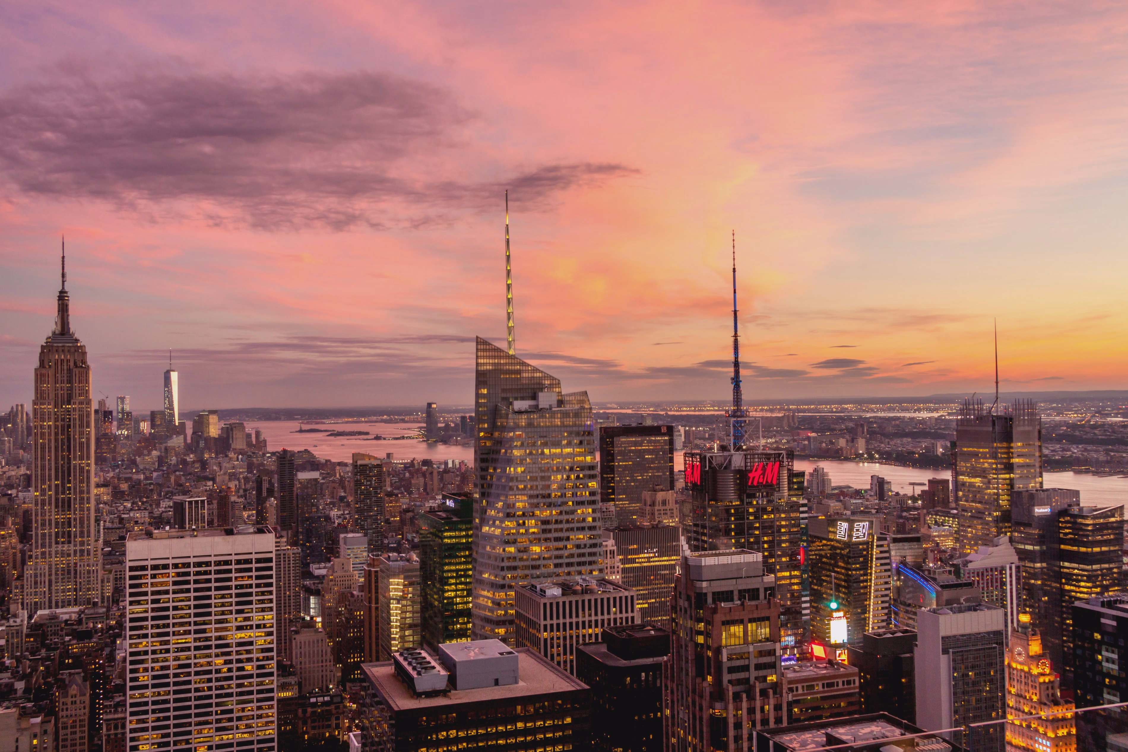 Manhattan’s Midtown skyline glows beneath a pink-orange sunset, with the Empire State Building rising among illuminated towers.