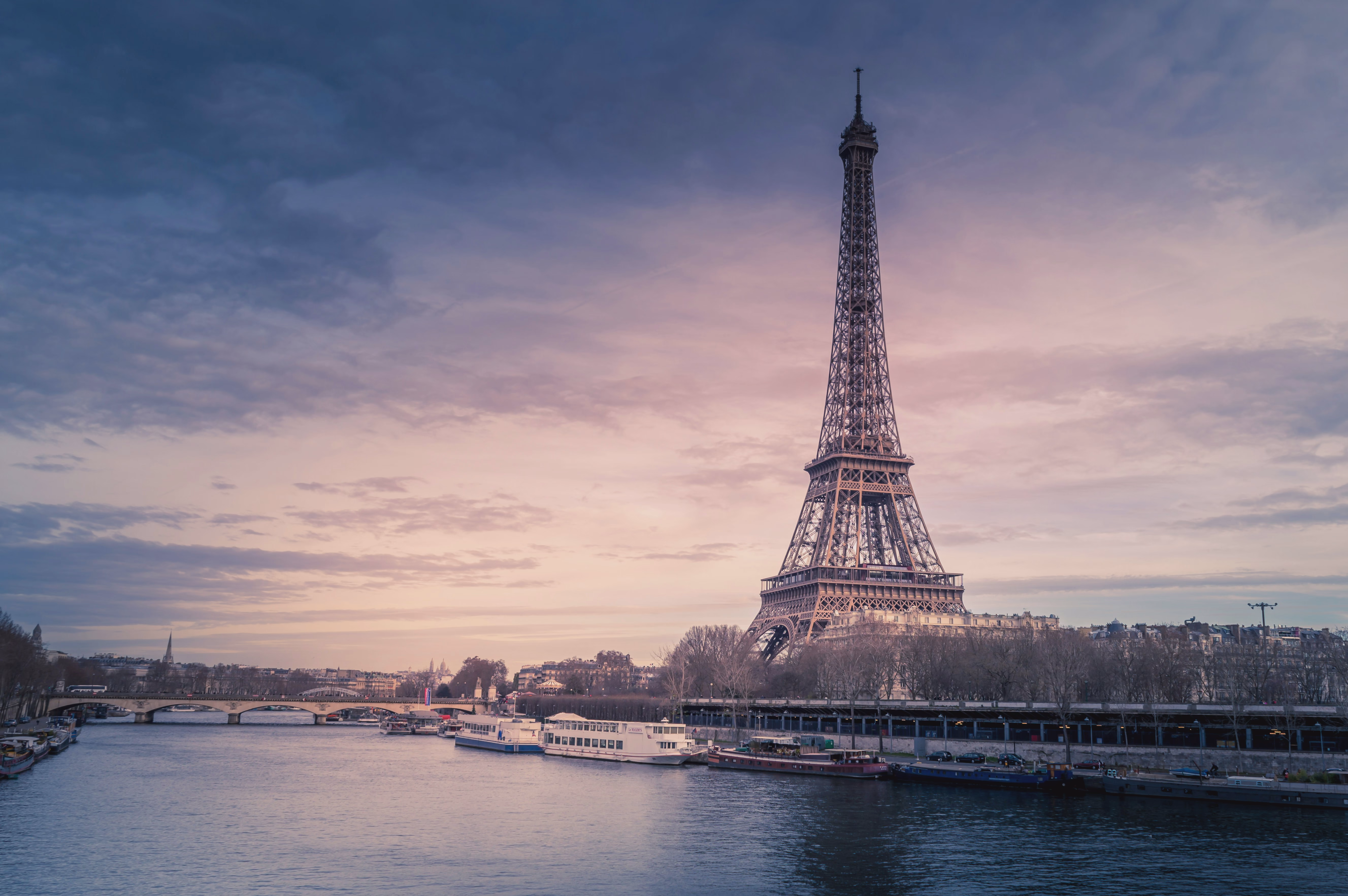 The Eiffel Tower rises above the Seine and Paris rooftops beneath a soft pink winter sky.